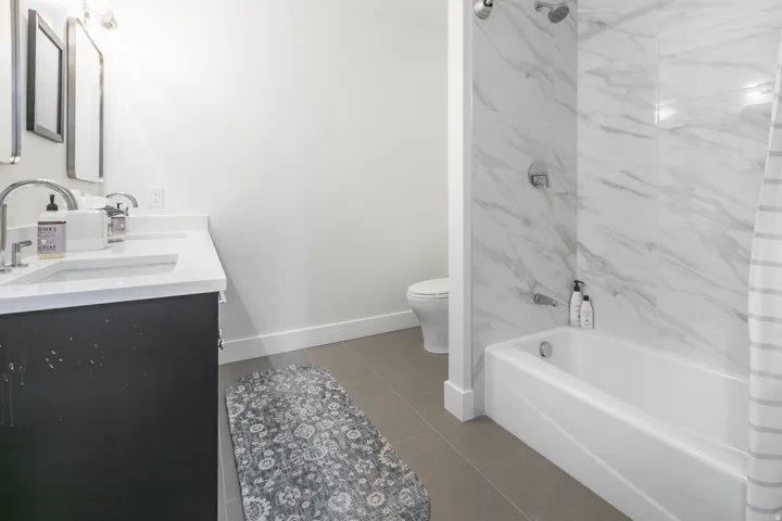 Bathroom featuring a dual-sink vanity with white countertops, a deep soaking tub, a tiled shower surround with a rainfall showerhead, and neutral floor tiling