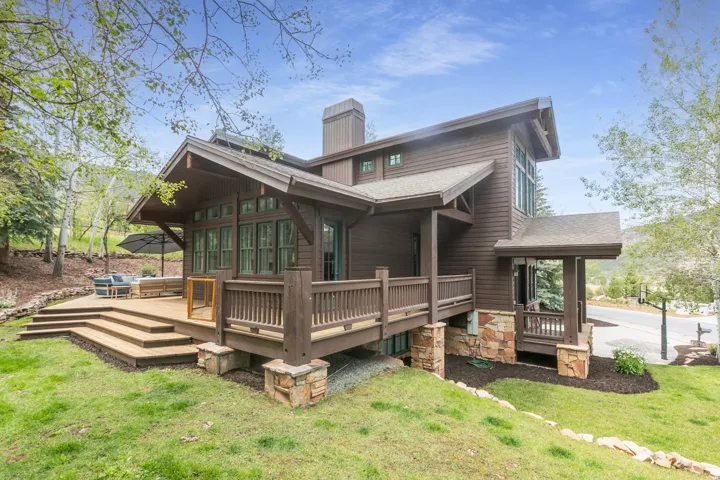 Brown siding exterior with a multi-level wood deck, stone accents, extensive windows, and a covered porch entry