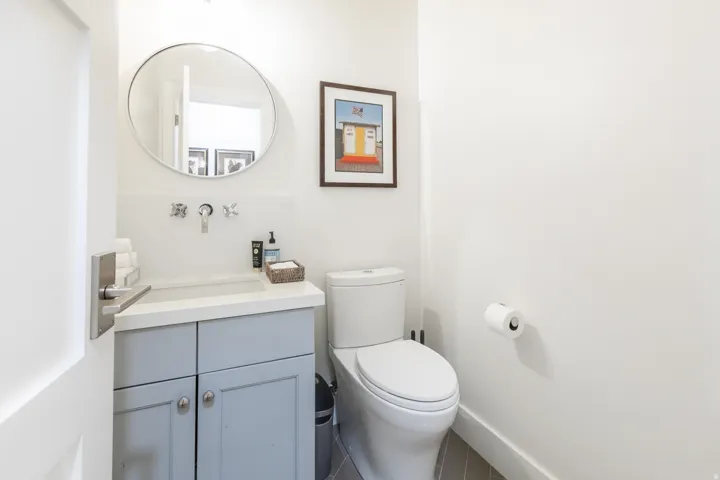 Compact bathroom featuring a white toilet, light gray vanity with a single basin, and a circular mirror