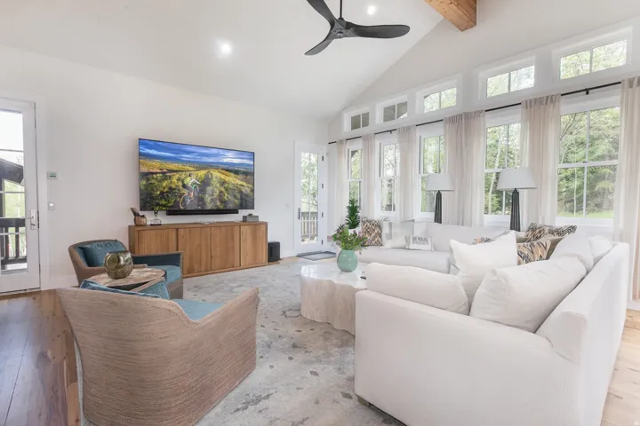 Vaulted ceiling with exposed wood beam, wood-finish flooring, and a wall of windows featuring transom accents