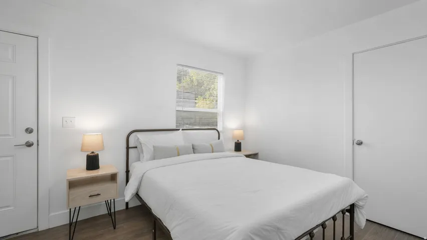 Bedroom featuring wood-finish flooring, white walls, and a window with horizontal blinds