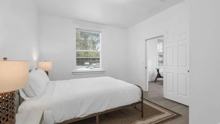 Bedroom featuring light gray wood-finish flooring, white walls, and a double-hung window with white trim