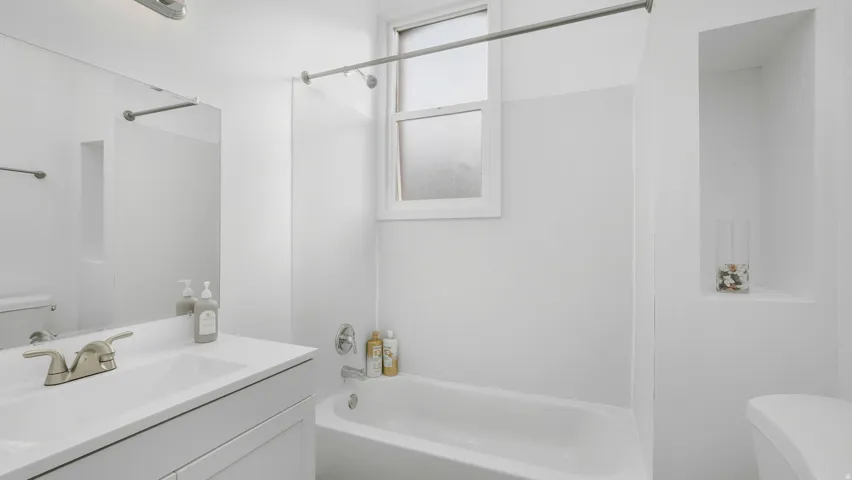 White bathroom featuring a single vanity with integrated sink, brushed nickel faucet, and overhead lighting