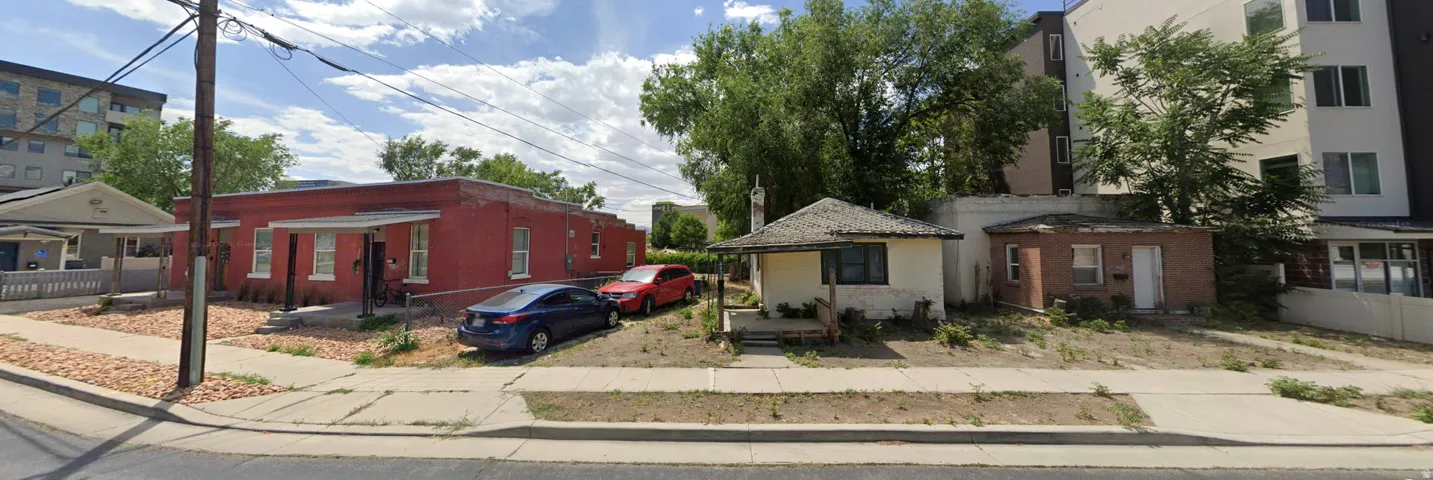 Red brick building with multiple entryways and prominent white trim, featuring a partial gravel front yard and an adjacent paved sidewalk