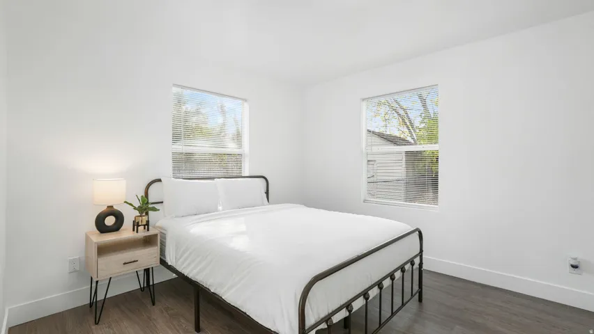 Bedroom featuring two windows with horizontal blinds, wood-finish flooring, white baseboards, and white painted walls