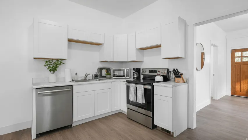 Kitchen featuring white shaker cabinetry, stainless steel appliances, light-toned countertops, and wood-finish flooring