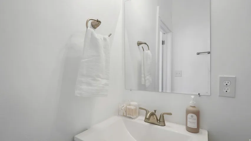 White sink basin with a brushed nickel faucet, an unframed wall mirror, and a wall-mounted towel ring