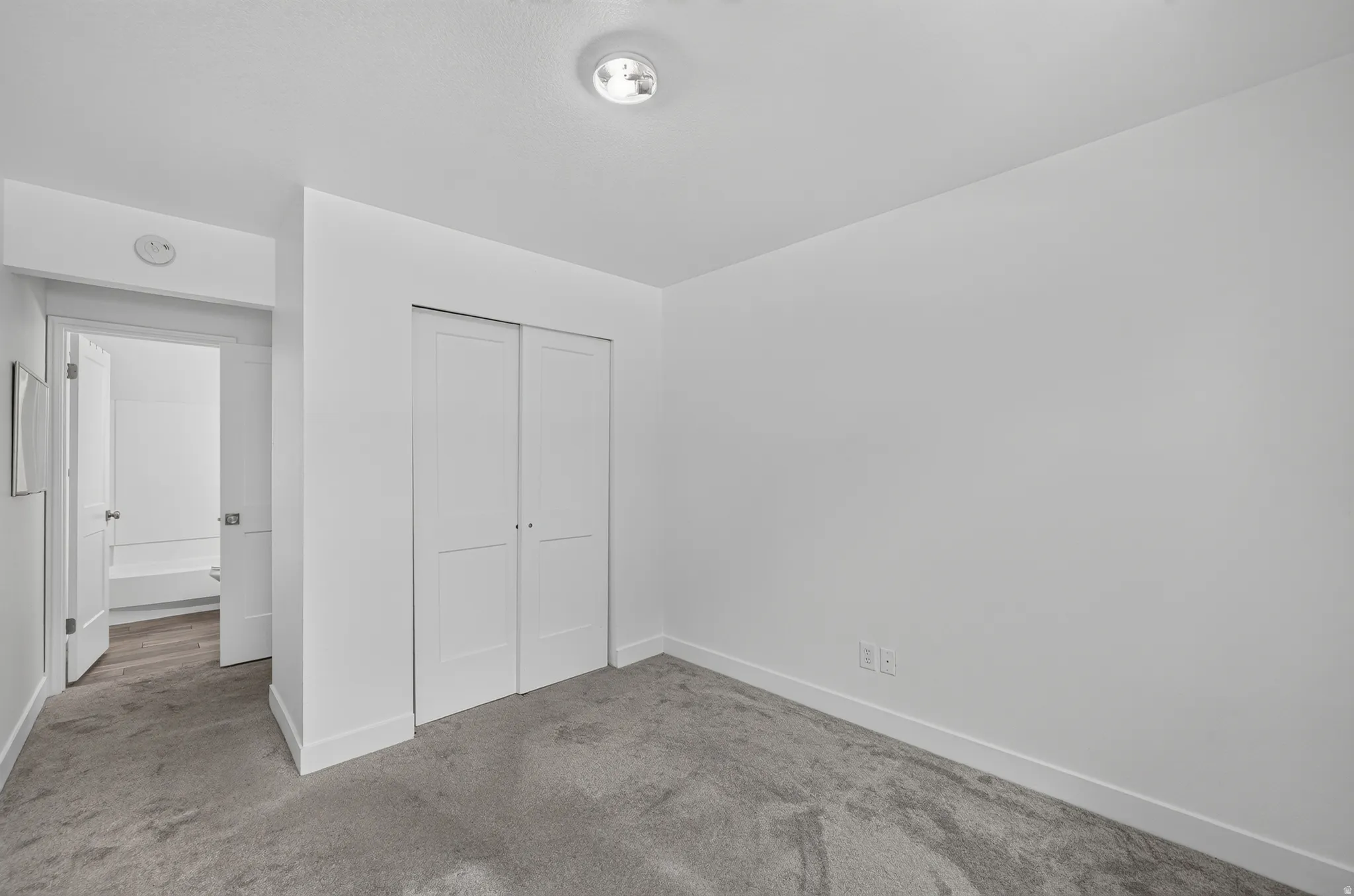 Carpeted room featuring white walls, white bi-fold closet doors, and white baseboards