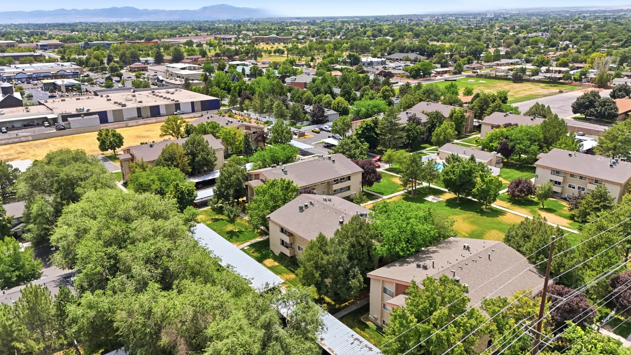 Aerial perspective showcasing multiple residential buildings with pitched roofs, surrounded by extensive green spaces and mature trees