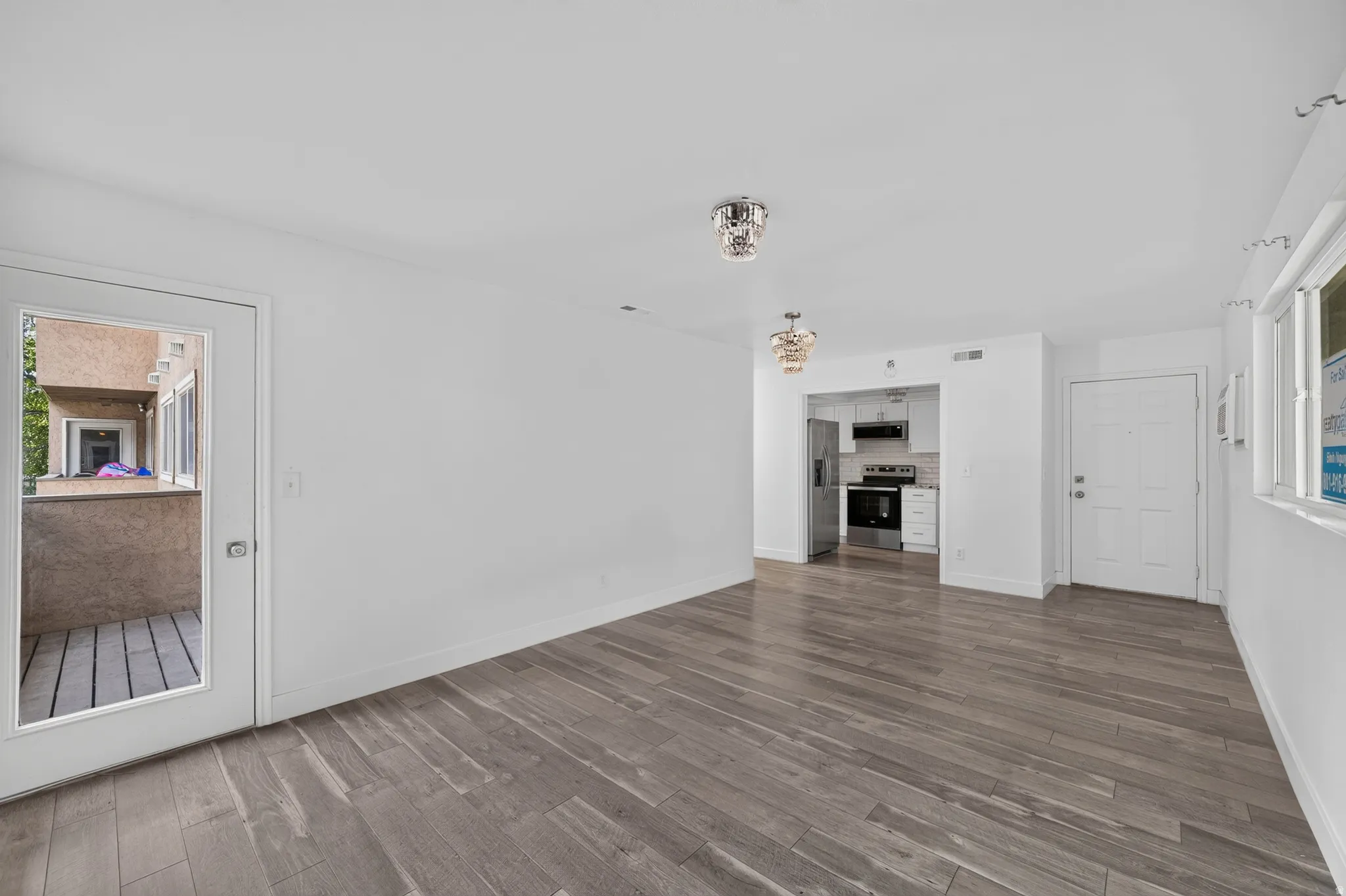 Spacious room featuring wood-finish flooring, white walls, and a glass-paneled door opening to a private balcony