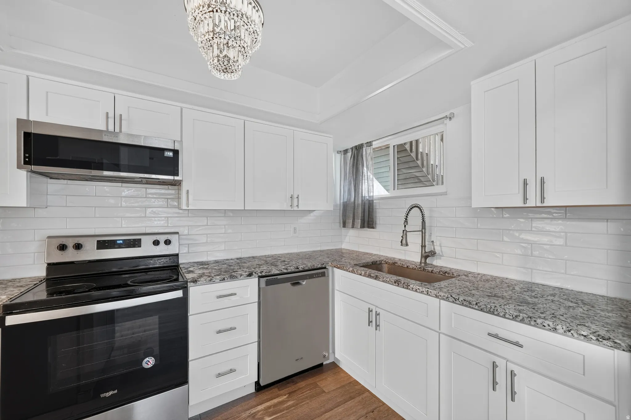 Updated kitchen featuring white shaker cabinetry, granite-finish countertops, stainless steel appliances, a subway tile backsplash, and wood-finish flooring
