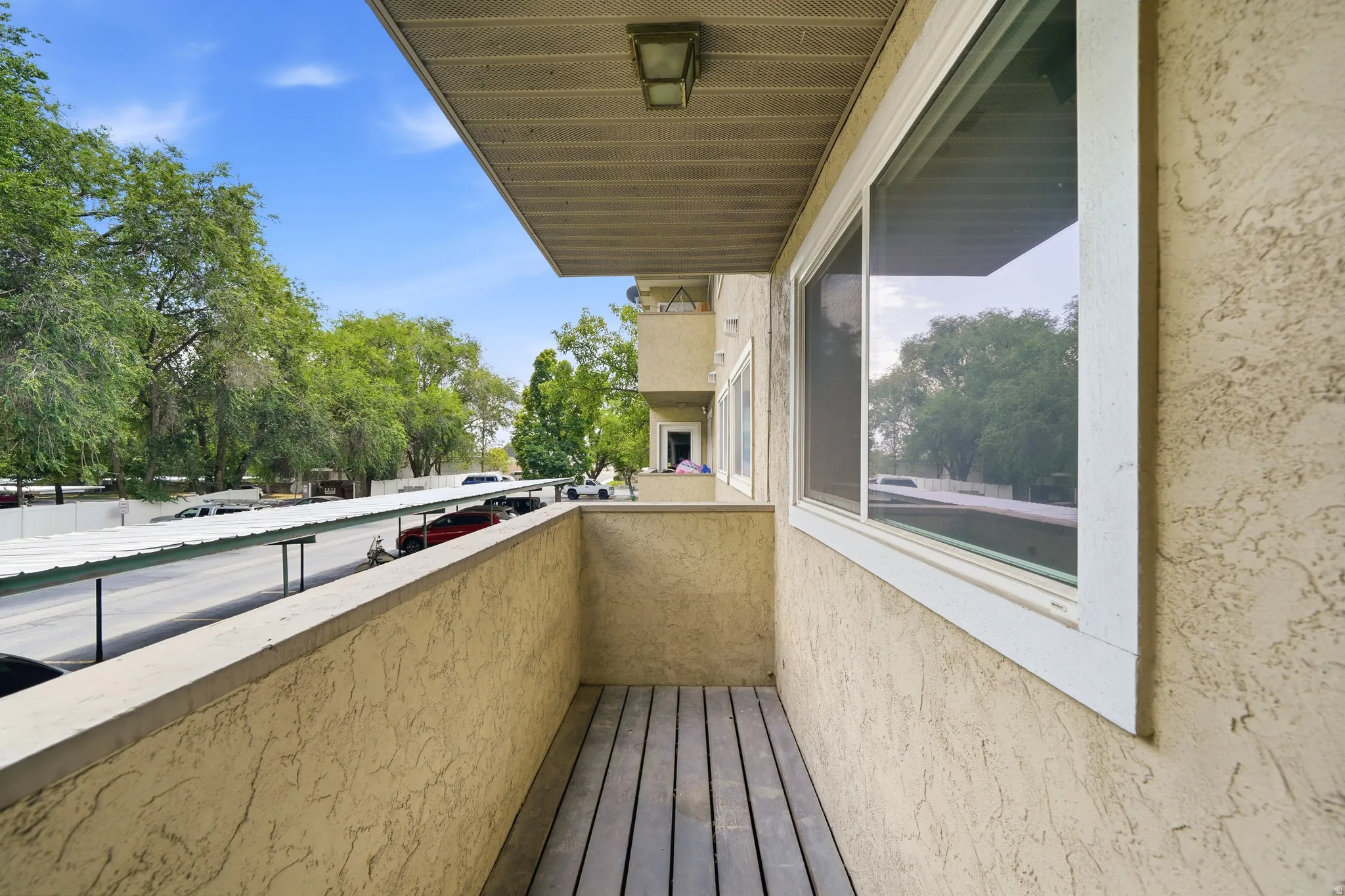 Exterior balcony featuring wood-finish flooring, stucco siding, and an overhead soffit with an attached light fixture