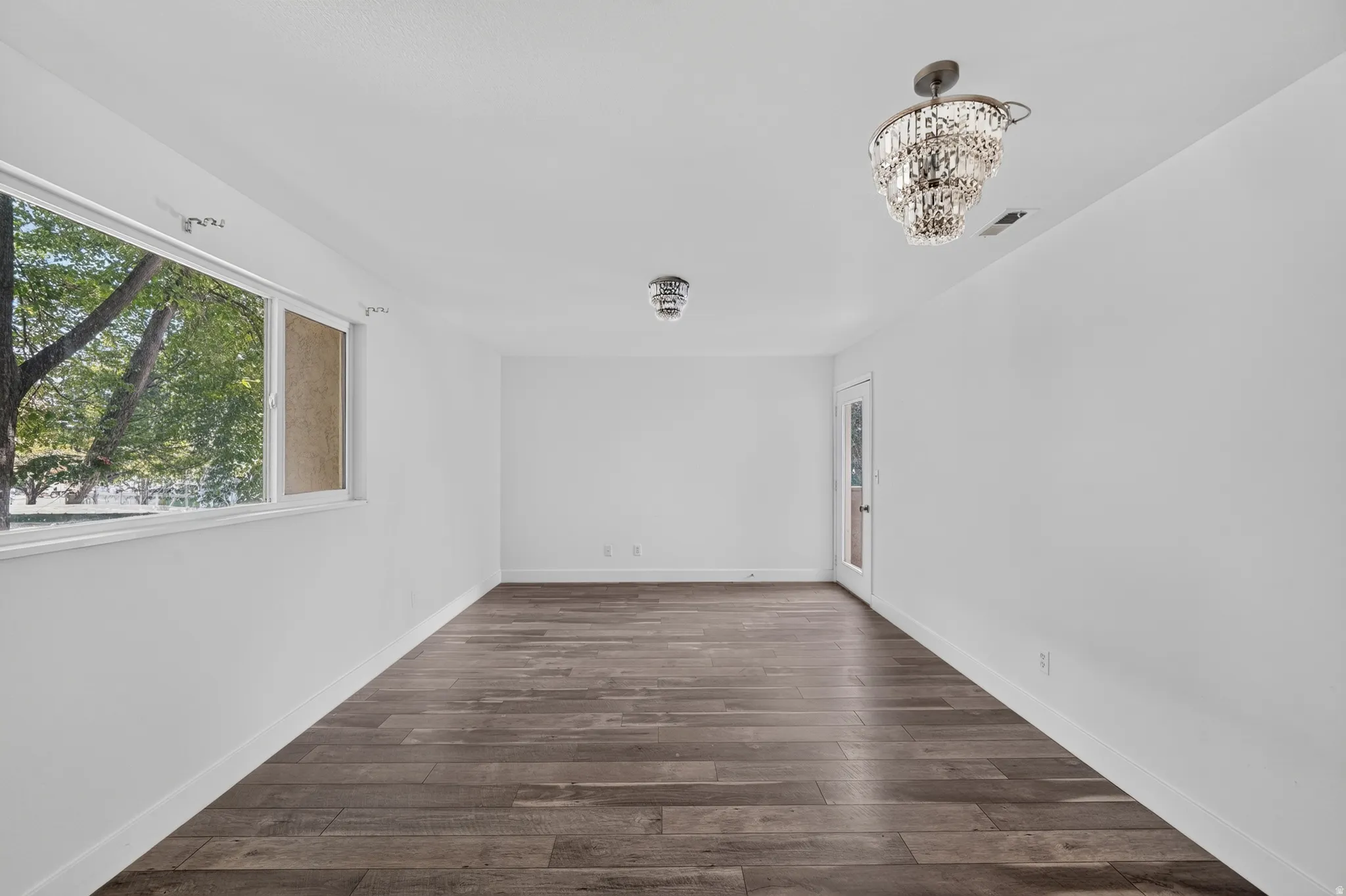 Spacious room featuring wood-finish flooring, white walls, and a large window