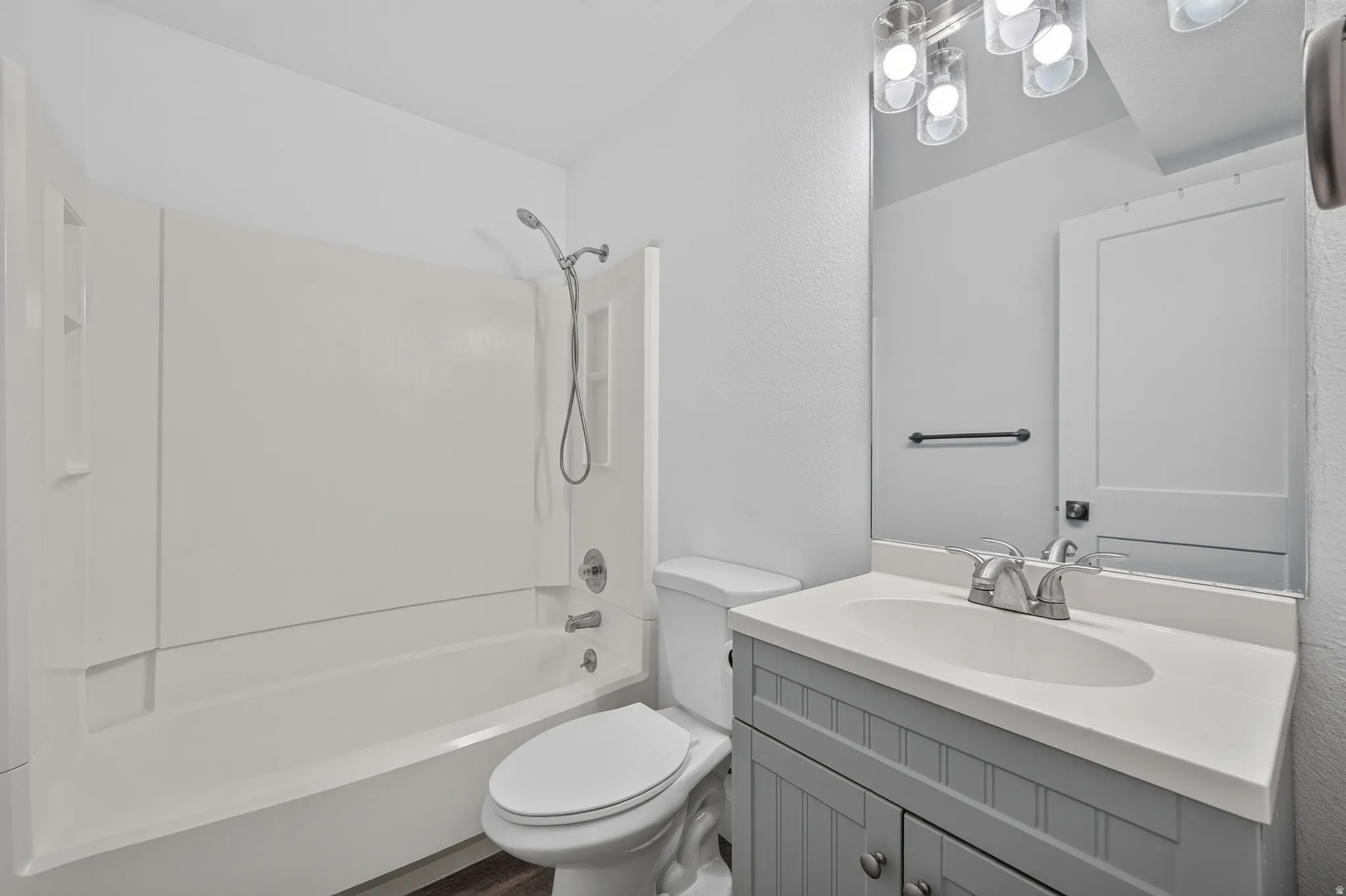 Bathroom featuring a white tub/shower combination with a handheld showerhead, a toilet, and a vanity with a light gray cabinet and white countertop
