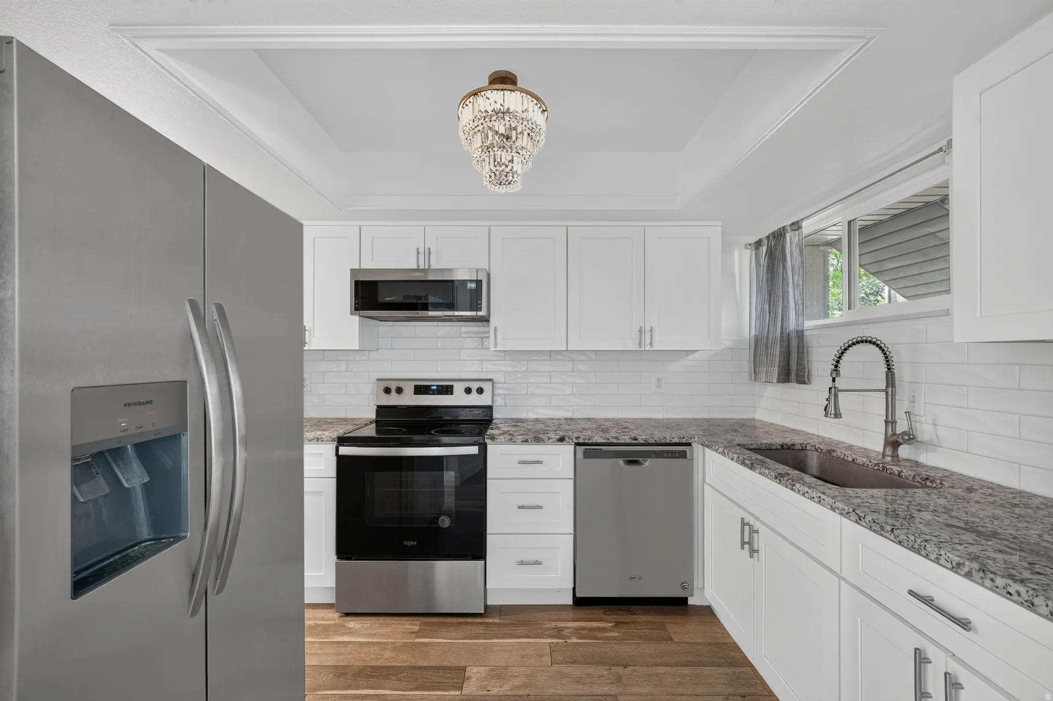 Kitchen featuring white shaker cabinetry, stainless steel appliances, speckled countertops, subway tile backsplash, and wood-finish flooring