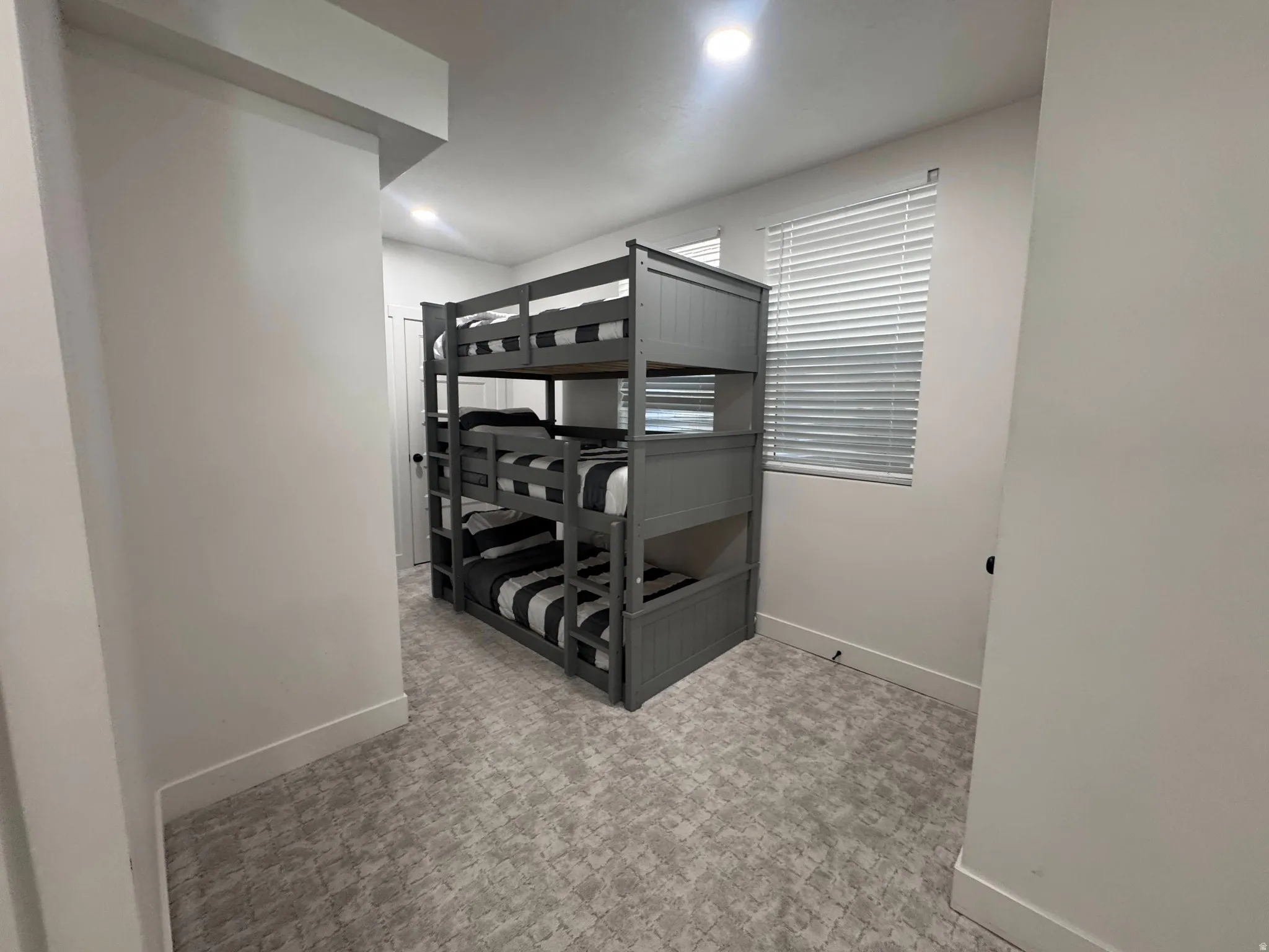 Room featuring textured grey carpet, white walls, and a window with horizontal blinds