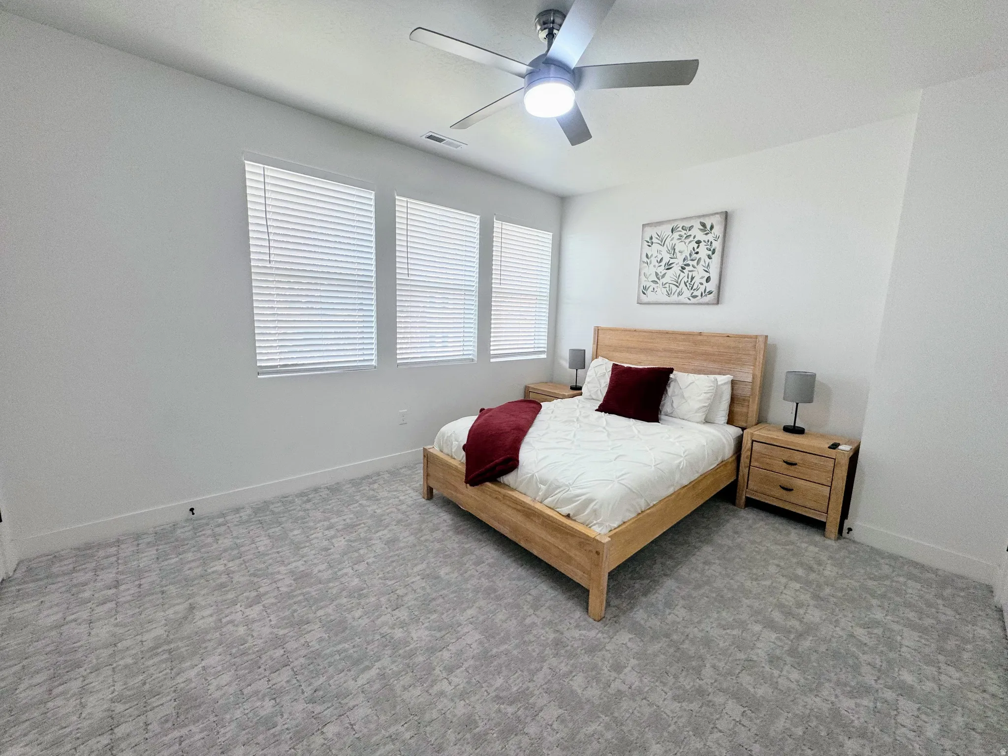 Room featuring three windows with blinds, a ceiling fan with light fixture, and patterned carpeting