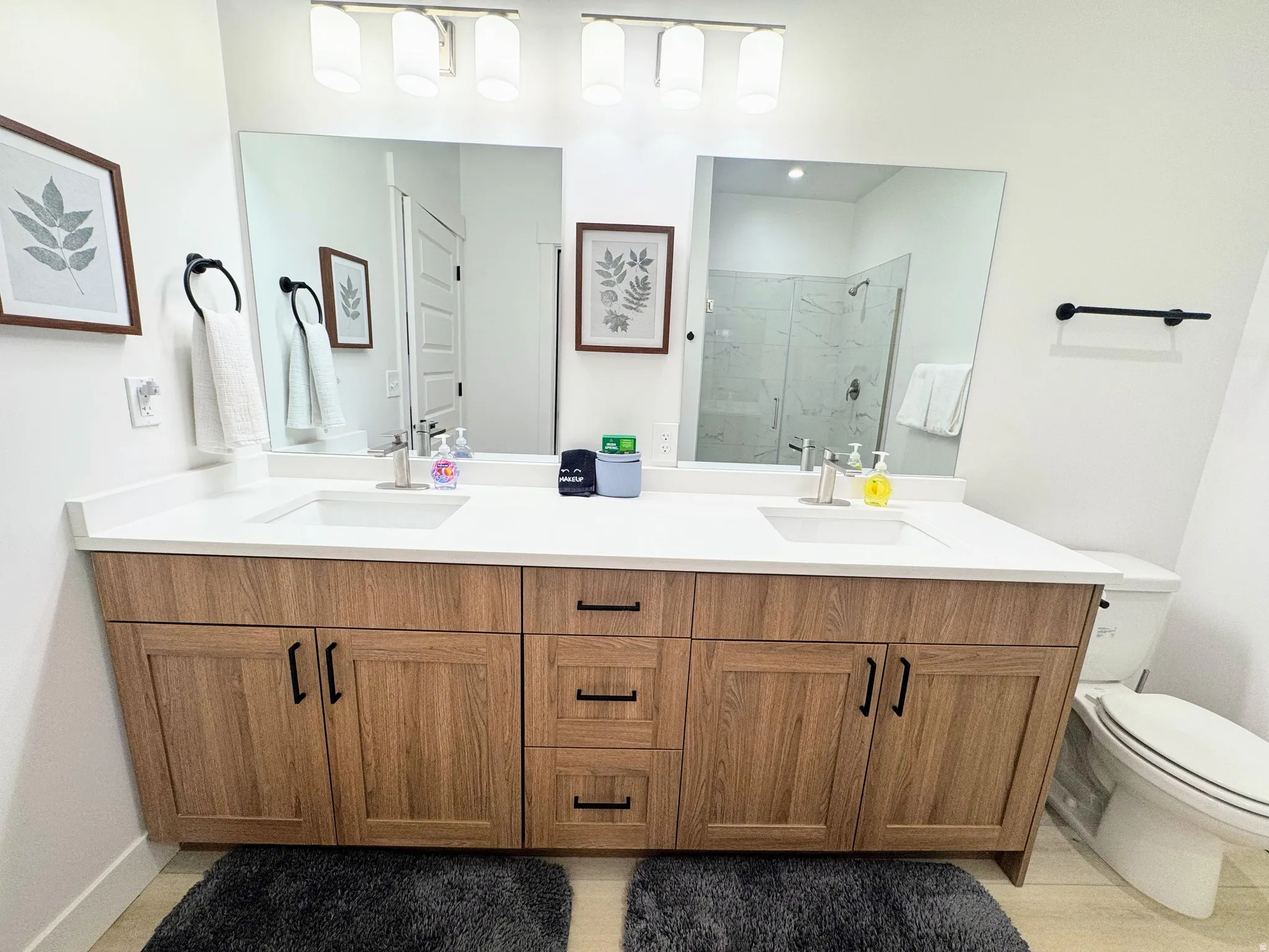 Dual vanity featuring wood-finish cabinetry with matte black hardware, white countertops, and integrated sinks