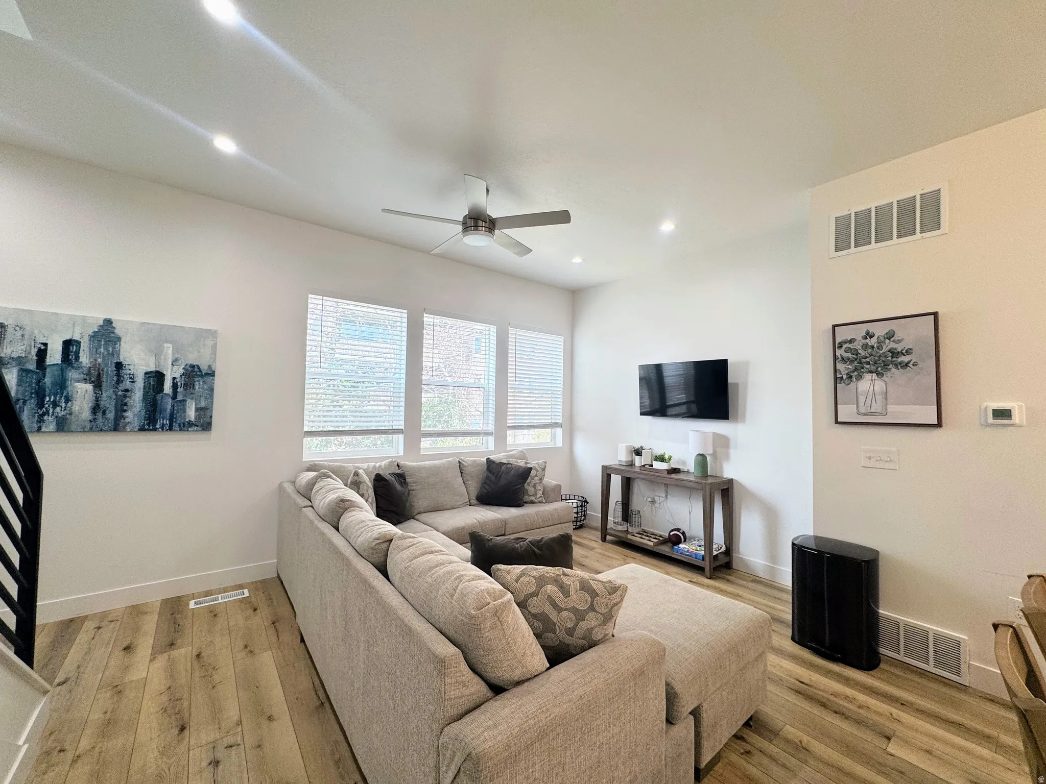 Spacious living area featuring wood-finish flooring, ample natural light from multiple windows, recessed ceiling lighting, and a ceiling fan