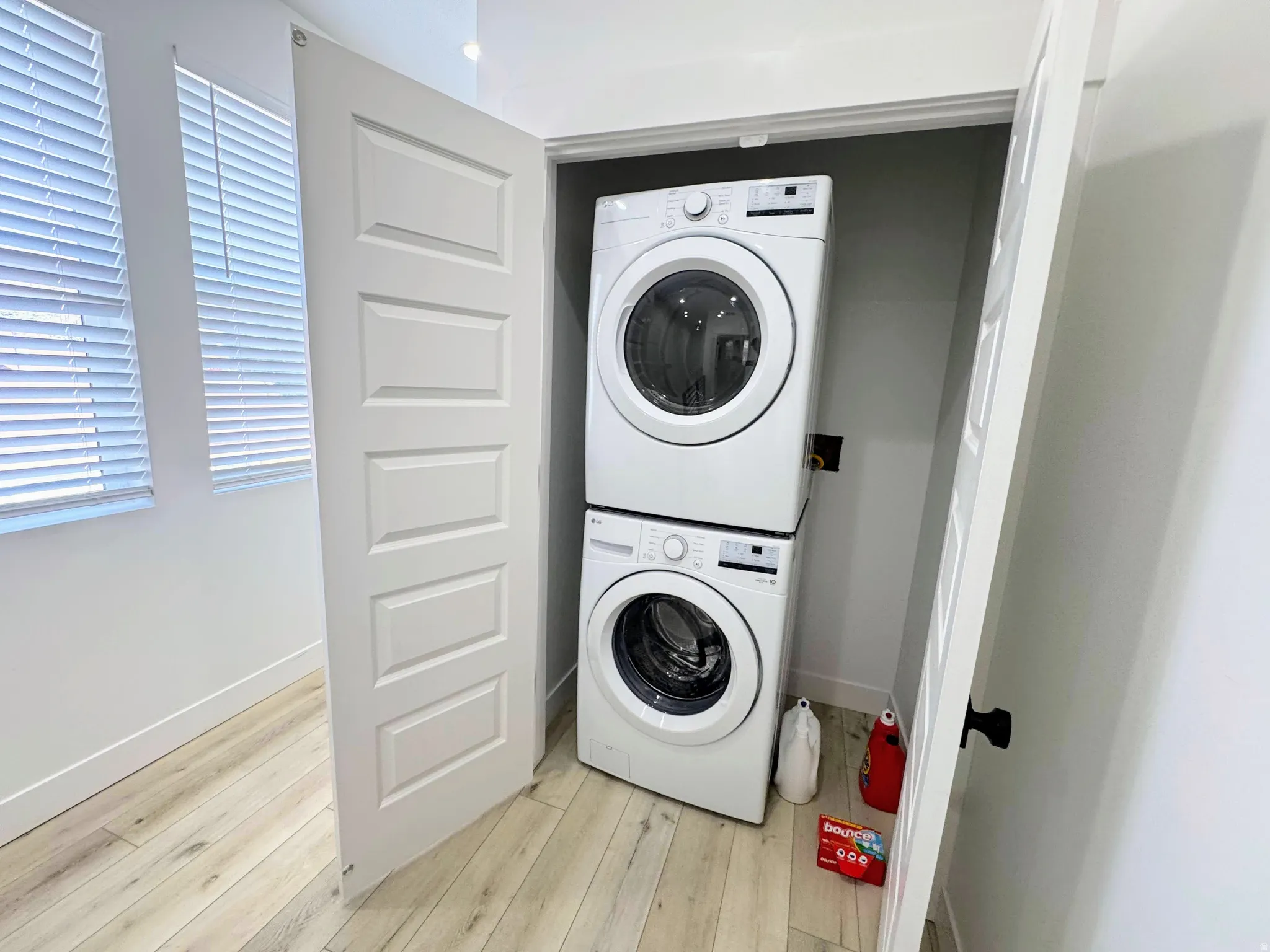 Dedicated laundry closet with stacked washer and dryer, wood-finish flooring, and horizontal blinds