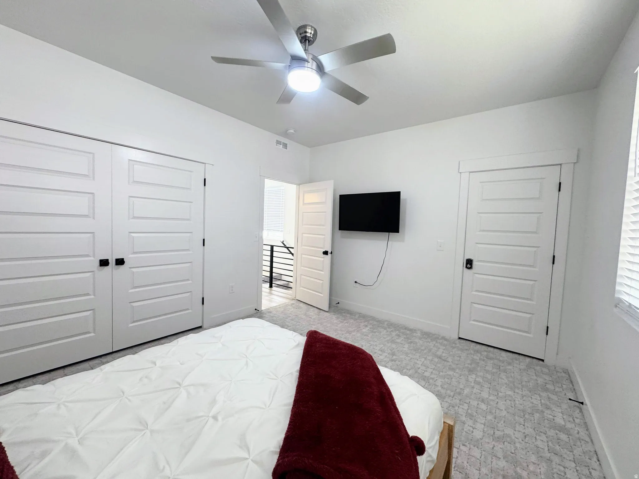 Bedroom featuring a ceiling fan with integrated lighting, paneled doors with matte black hardware, and patterned carpeting