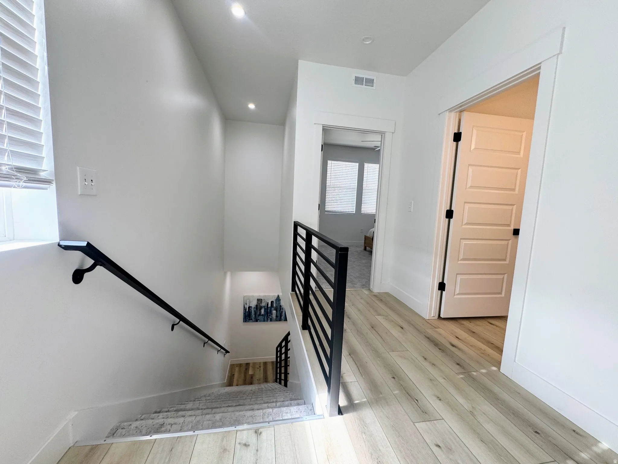 Upper-level hallway featuring wood-finish flooring, recessed lighting, and a modern black metal stair railing