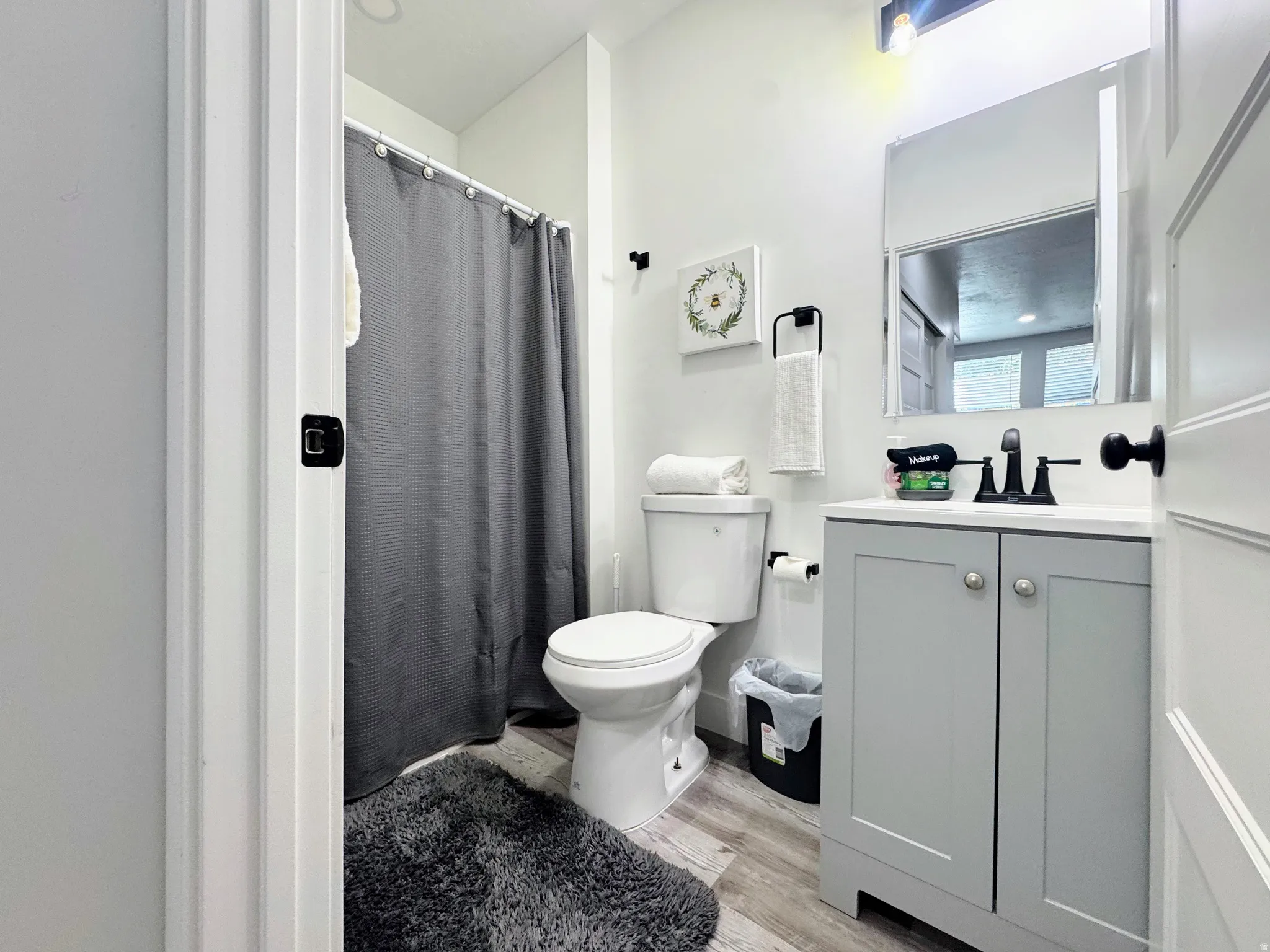 Bathroom featuring a single vanity with a gray cabinet base and white countertop, a wall-mounted mirror, a toilet, and wood-finish flooring