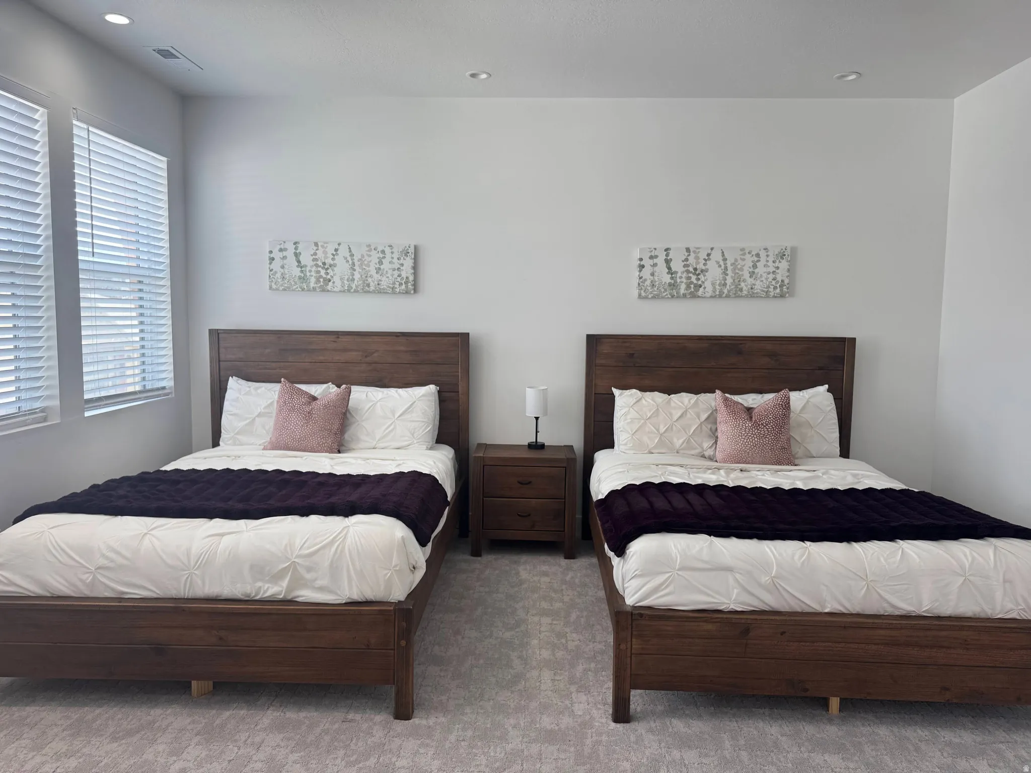 Bedroom featuring twin wood-finish bed frames, a shared wood-finish nightstand, recessed lighting, and dual windows with blinds