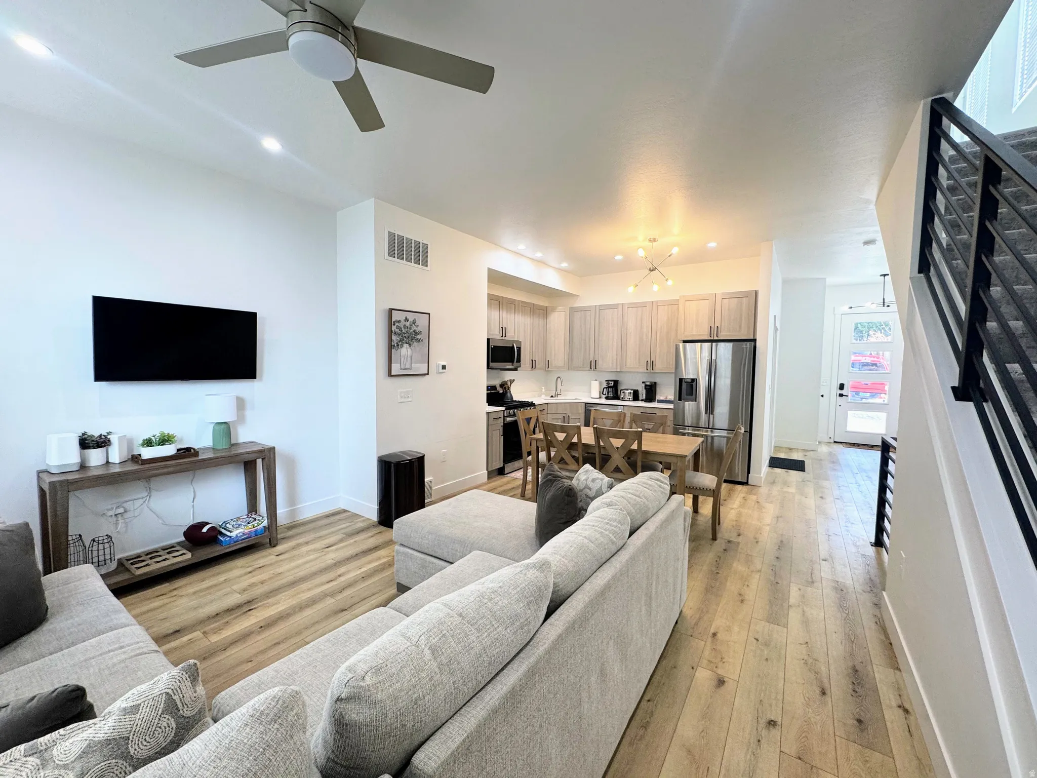 Open-concept living area featuring wood-finish flooring, recessed lighting, a ceiling fan, and a kitchen with stainless steel appliances and light wood-tone cabinetry