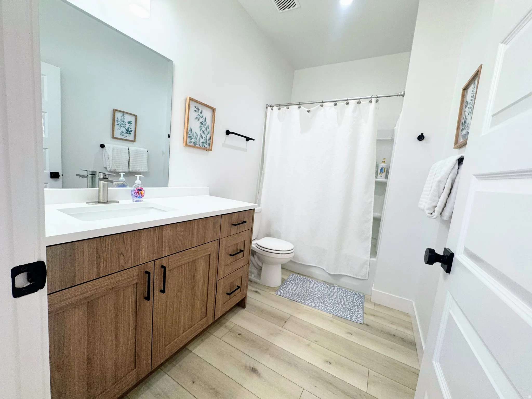 Bathroom featuring a wood-finish vanity with a light-colored countertop, integrated sink, and black hardware