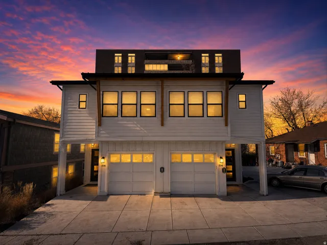 Modern exterior featuring white horizontal siding, a dark trim roofline, wooden support beams, multiple large windows, and a two-car garage