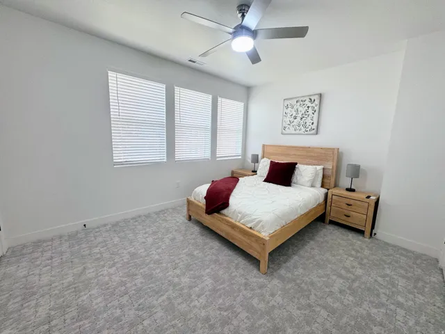 Room featuring three windows with blinds, a ceiling fan with light fixture, and patterned carpeting