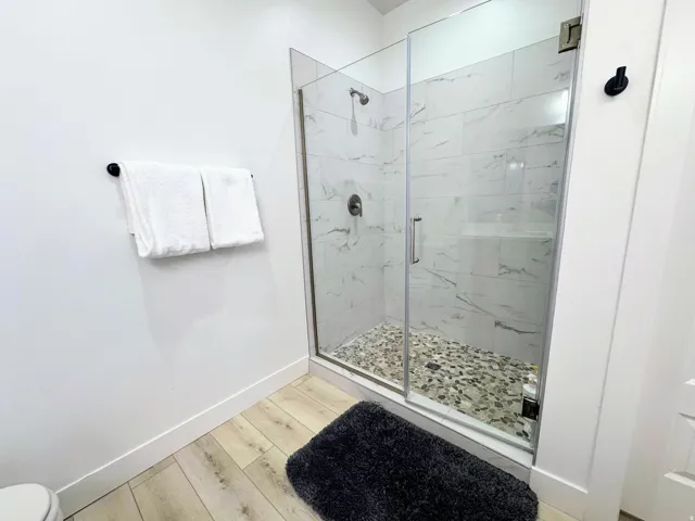 Walk-in shower featuring a glass enclosure, white marble-look subway tile surround, pebble tile shower floor, and a dark bronze shower fixture