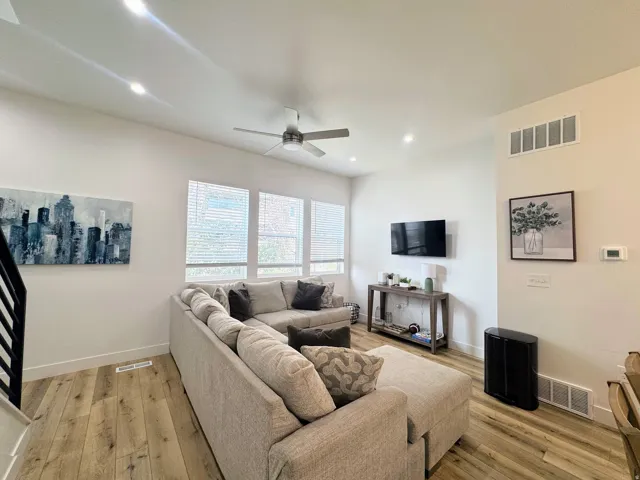 Spacious living area featuring wood-finish flooring, ample natural light from multiple windows, recessed ceiling lighting, and a ceiling fan