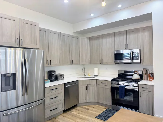 Modern kitchen featuring light wood-finish cabinetry with black hardware, stainless steel appliances, white countertops, and a subway tile backsplash