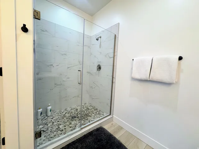 Glass-enclosed shower featuring large format wall tiling with subtle veining and a pebble-stone floor