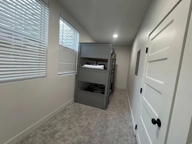 Alcove featuring two windows with horizontal blinds, light-toned patterned carpet, a built-in bunk bed structure, a white paneled interior door with a black knob, and recessed ceiling lighting