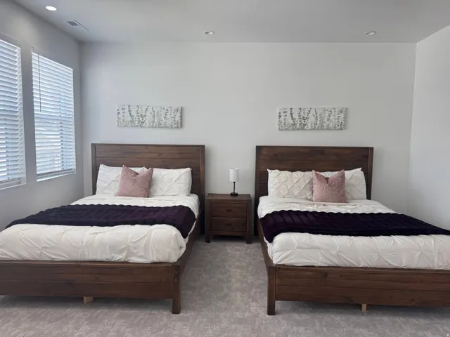 Bedroom featuring twin wood-finish bed frames, a shared wood-finish nightstand, recessed lighting, and dual windows with blinds
