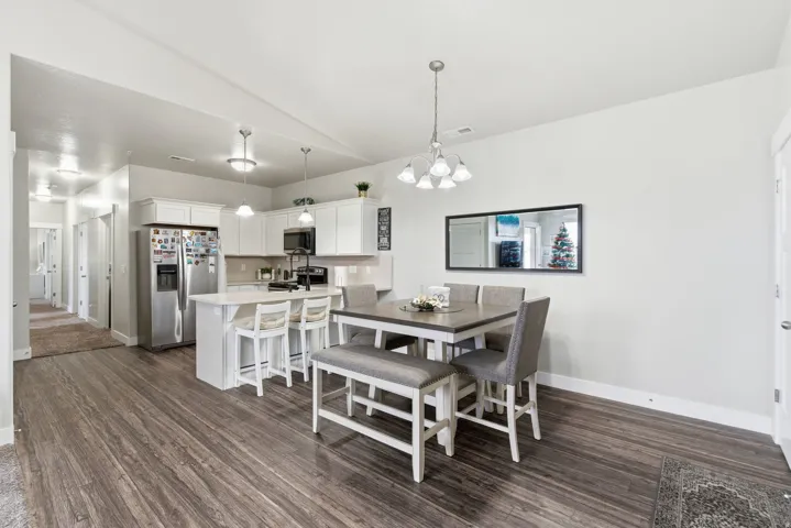 Open-concept kitchen and dining area featuring wood-finish flooring, white cabinetry, a kitchen island with seating, pendant lighting, and a dining light fixture
