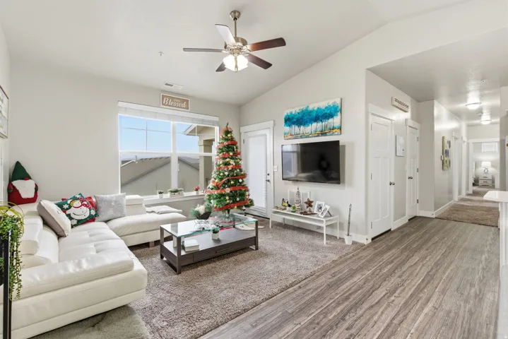 Living area featuring vaulted ceilings, a ceiling fan with integrated lighting, wood-finish flooring, a large window, and a white paneled door