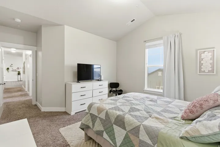 Spacious room featuring vaulted ceilings, light-toned walls, and a large window with roller shades