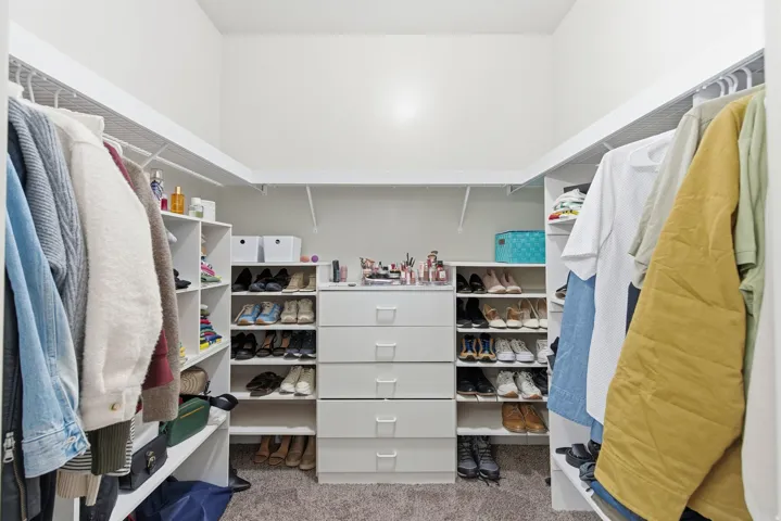 Walk-in closet featuring built-in white shelving, multiple hanging rods, and a central dresser unit with five drawers