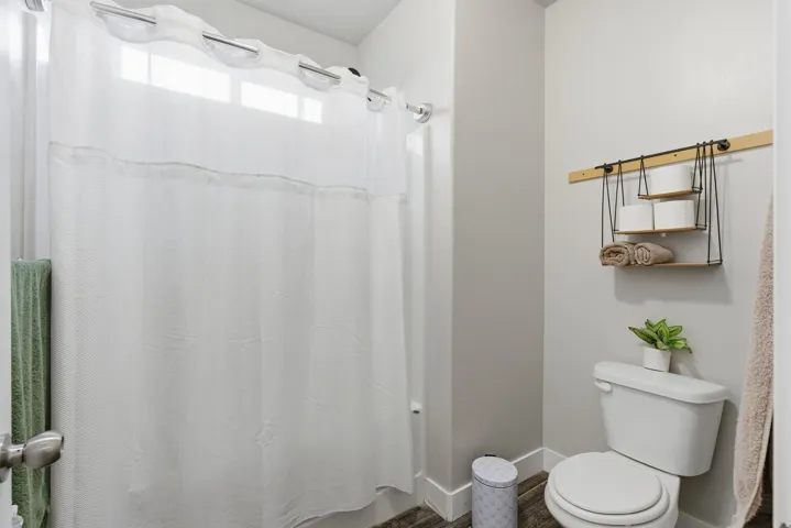 Full bathroom featuring a white toilet, gray walls, white baseboards, and wood-finish flooring