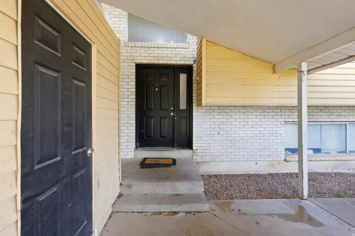 Entryway featuring a black paneled door with a sidelight, white brick façade, and an overhead awning