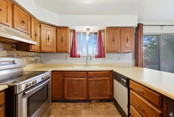 Kitchen featuring wood cabinetry, light-toned countertops, tile flooring, stainless steel range, and a built-in dishwasher