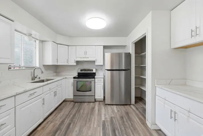 Contemporary kitchen featuring white cabinetry, light countertops, wood-finish flooring, a stainless steel appliance suite, and a built-in pantry