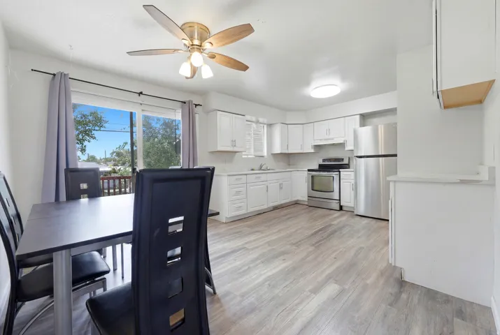 Open-concept kitchen and dining area featuring light wood-finish flooring, white cabinetry, stainless steel appliances, and a ceiling fan with integrated lighting