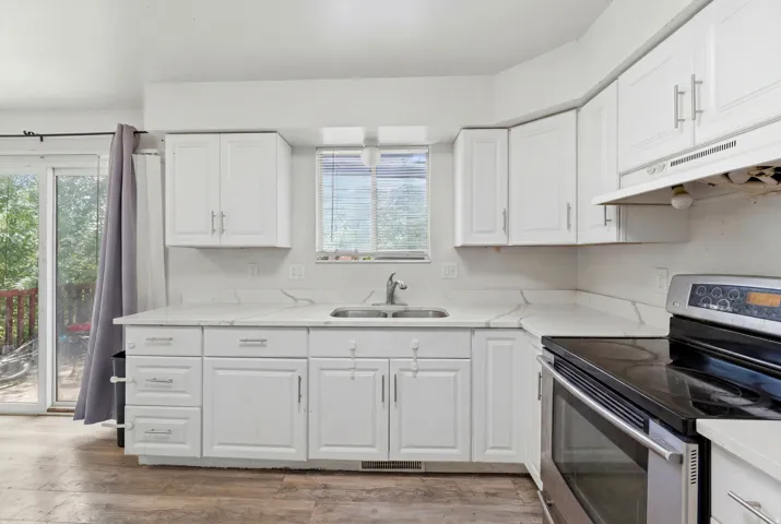 Kitchen featuring white cabinetry with brushed nickel hardware, a stainless steel double basin sink, and wood-finish flooring