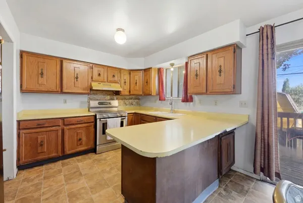 Kitchen featuring wood cabinetry, light-toned countertops, tile flooring, and a stainless steel range
