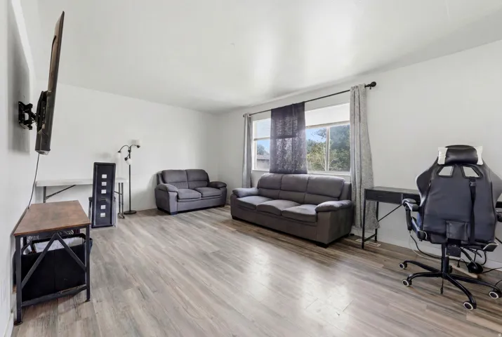 Spacious room featuring light wood-finish flooring, white painted walls, and a large window with privacy blinds